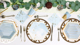A set of party tables with golden blue hued plates and cutlery, arranged on a table with decorative flowers and a geometric pattern.