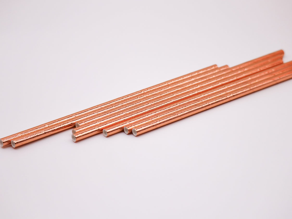A set of metallic biodegradable paper straws in rose gold color, laid out on a white background.